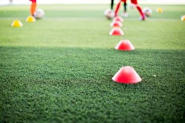 Kırmızı koni işaretleyicisi için seçici odak noktası yeşil suni sahada futbol eğitim ekipmanları ve bulanık çocuk oyuncuların eğitim geçmişi. Futbol akademisinin eğitim sınıfı için malzeme..