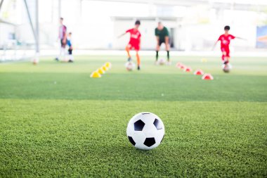 Yeşil suni sahada futbol topu ve bulanık çocuk futbol takımı eğitimi. Bulanık futbolcu çocuk futbol akademisinde futbol ekipmanıyla işaret konileri arasında koşuyor..