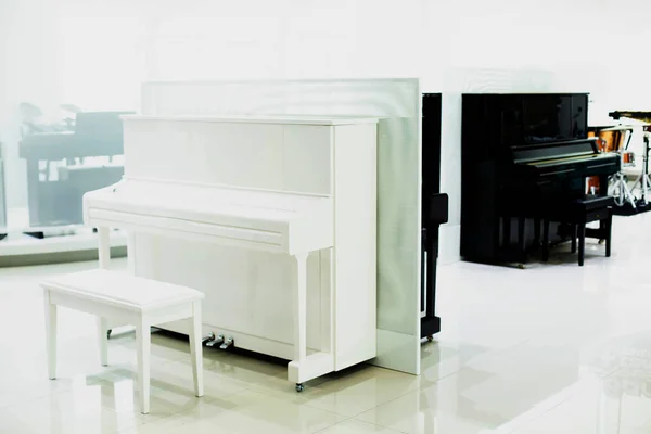 White piano with blurry black piano in musical showroom at musical instrument store.