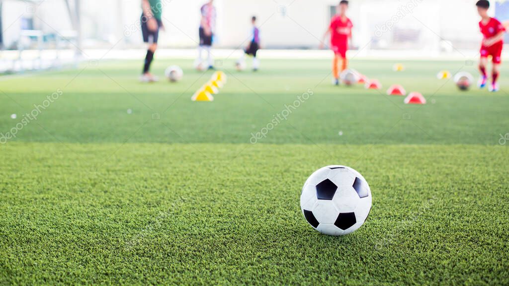 Soccer ball on green artificial turf with blurry kid soccer team training. Blurry kid soccer player jogging between marker cones and control ball with soccer equipment in football academy.