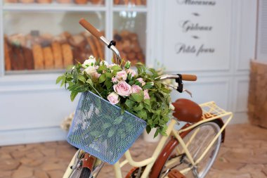 pastel renklerde duvara karşı gül sepeti ile eski bisiklet. Bitkiler ve çiçekler için dekoratif bisiklet standı. Güzel romantik manzara: kafe yakınında çiçekler ile vintage hasır sepeti.