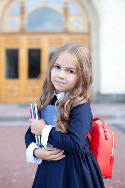 Elinde kitap, kalem ve okul çantası olan liseli kız. Okula dönelim. İlkokul öğrencisiyim. Dersler başlıyor. Okul binasının yakınında küçük bir kız. Eğitim kavramı. 