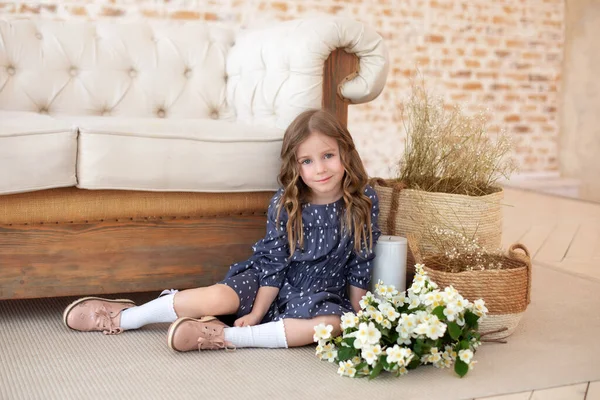 Bir buket yasemin çiçeğiyle gülümseyen kıvırcık saçlı kız sonbahar oturma odasındaki kanepede oturur. İskandinav iç mimarisi. Kutlama. Anneler Günü. Anne için bir buket çiçekli çocuk.