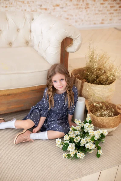 Bir buket yasemin çiçeğiyle gülümseyen kıvırcık saçlı kız sonbahar oturma odasındaki kanepede oturur. İskandinav iç mimarisi. Kutlama. Anneler Günü. Anne için bir buket çiçekli çocuk.