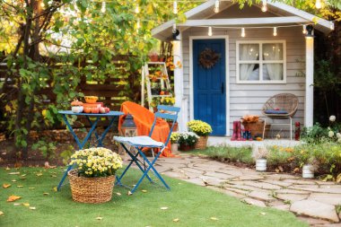 Şükran Günü 'nde sonbahar süslemeleri olan güzel bir sundurma evi. Bahçe masası ve sonbahar bahçesinde elmalı ve balkabaklı sandalyeler. Teraslı ve retro ampullü çelenkler. Cadılar Bayramı. İç konforlu veranda