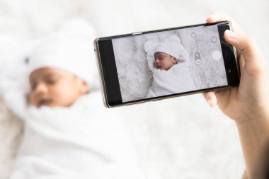 Annenin el ele tutuşması akıllı telefon kullanımı fotoğraf çekmek için sevimli yeni doğan bebek hatıralar ve sosyal ağda poz vermek için.