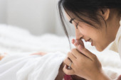 Asiatische junge Mutter küsst Füße des niedlichen Neugeborenen schlafend. Muttertagskonzept.