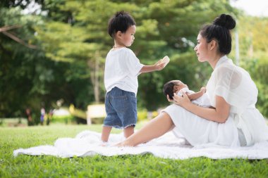 Güzel Asyalı genç anne ya da yeni doğmuş bebek ve oğlu olan bekar anne parkta etkinlikler düzenliyor ve dinleniyorlar. Çocuk ve aile büyütmenin eş ve anne görevi kavramı.