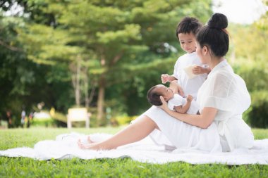 Güzel Asyalı genç anne ya da yeni doğmuş bebek ve oğlu olan bekar anne parkta etkinlikler düzenliyor ve dinleniyorlar. Çocuk ve aile büyütmenin eş ve anne görevi kavramı.