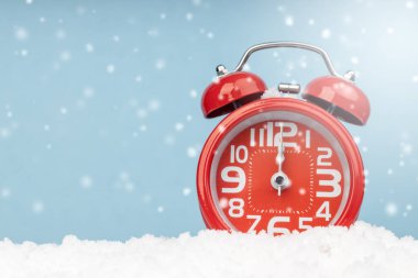 Sahte kar ve mavi arka plana yerleştirilmiş kırmızı alarm saati. Selamlamalarınız için alanı kopyalayın.