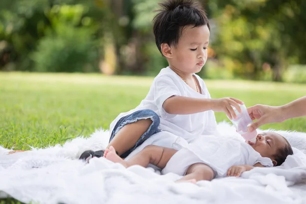 公園で息子と一緒にシングルマザーと娘のための休暇 庭の芝生の上で眠っている新生児の妹を母親が養うのを手伝っています — ストック写真