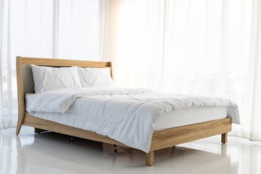 Tahta yatak beyaz perdeler ve yumuşak güneş ışığı ile çevrili boş odada beyaz çarşaflarla yatar. .