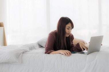 Çalışmak için dizüstü bilgisayar kullanan Asyalı bir kadın, eğitim, e-ticaret, yatağında sosyal medya. Corovavirus covid-19, evde kal, iş formu ev kavramı.