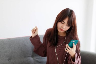 Güzel Asyalı kadın yatak odasında müzik dinlerken akıllı telefon kullanıyor. Evde kal, Coronavirus covid-19..