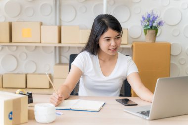 Evde çalışan Asyalı serbest kadın ve internet üzerinden küçük işletme girişimcisi KME 'yi kuruyor. Genç bayan sipariş sayısını kontrol etmek için dizüstü bilgisayar kullanıyor..