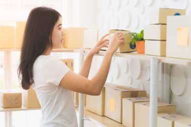 Evde çalışan Asyalı serbest kadın ve internet üzerinden küçük işletme girişimcisi KME 'yi kuruyor. Kadın gülümsüyor ve teslimatı hazırlıyor..