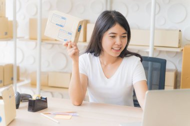 Evde çalışan Asyalı serbest kadın ve internet üzerinden küçük işletme girişimcisi KME 'yi kuruyor. Genç kadının portresi gülümsüyor ve teslimatı hazırlamak için paket kutusu hazırlıyor..