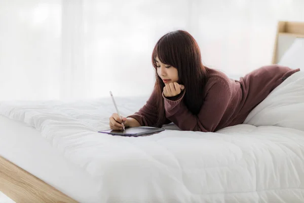Asian woman using tablet for working, educational, e-commerce, social media in her bed. corovavirus covid-19, stay at home, work form home concept.
