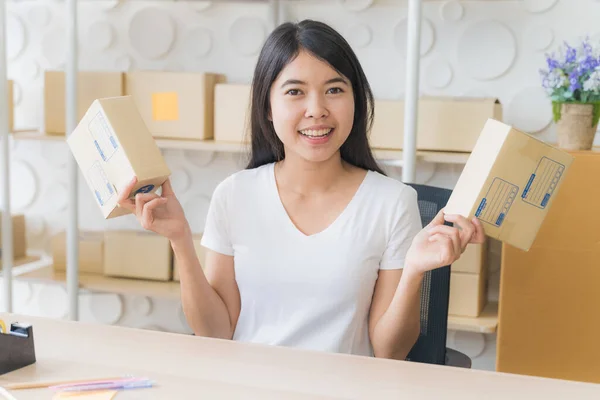 Asian freelance woman working at home and start up small business entrepreneur SME with internet online. Portrait of young woman is smiling and preparing package box to prepare the delivery for the customer.