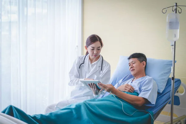 男性患者とアジアの女性医師は タブレットからの結果をチェックしています — ストック写真