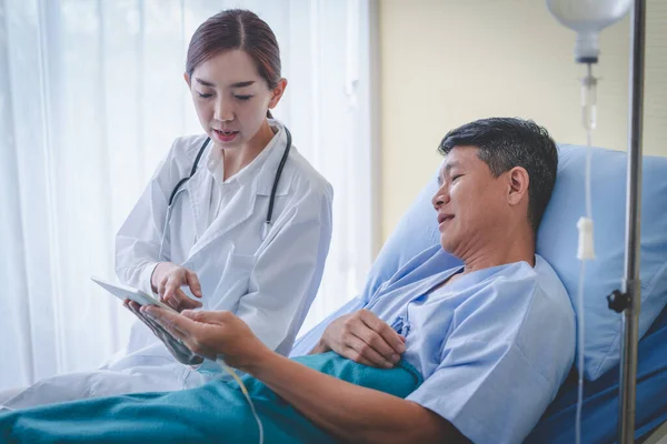 男性患者とアジアの女性医師は タブレットからの結果をチェックしています — ストック写真