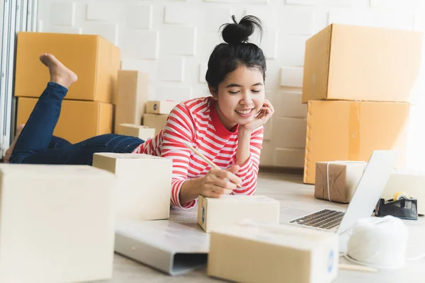Asian freelance woman working at home and start up small business entrepreneur SME with internet online. Women are preparing products in the packaging box to prepare for delivery to customers.