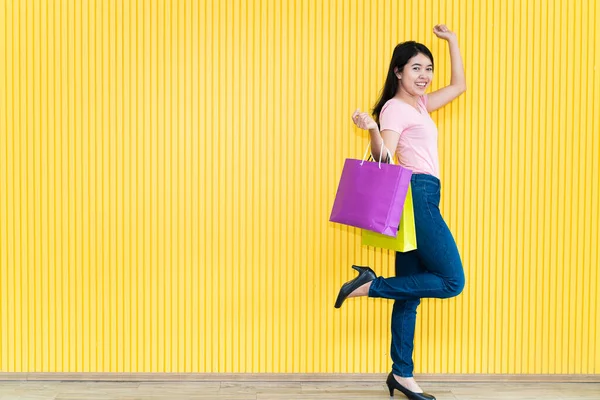 身穿粉色T恤和牛仔裤的亚洲年轻女子背着几个黄色背景的纸袋 购物概念 — 图库照片