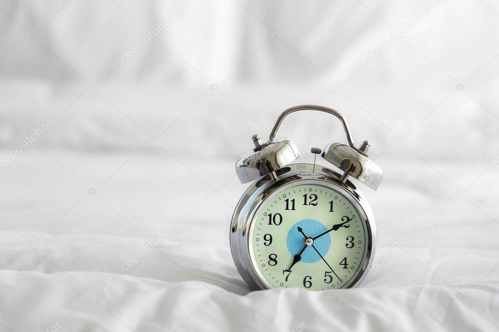 Alarm clock on white blanket in bed room.