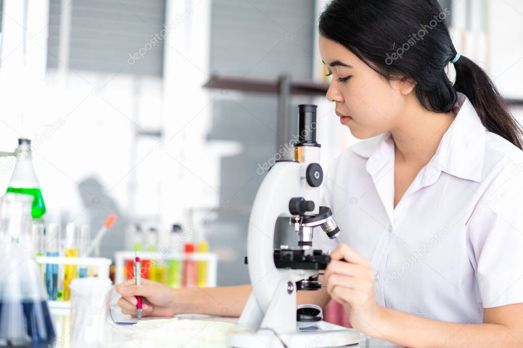 Asian girl students are doing science experiments with a microscope in a science lab.