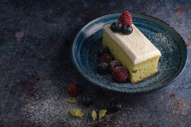Üzerinde yaban mersini, ahududu ve pas masasında mavi tabakta krema olan taze tereyağlı pasta manzarası. Lezzetli böğürtlenli peynirli kek. Durgun yaşam tarzı.