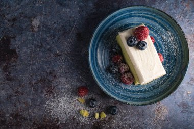 Üzerinde yaban mersini, ahududu ve pas masasında mavi tabakta krema olan taze tereyağlı pasta manzarası. Lezzetli böğürtlenli peynirli kek. Durgun yaşam tarzı.