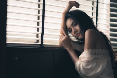 Jalousie 'nin yanında oturan beyaz elbiseli seksi genç kadın portresi