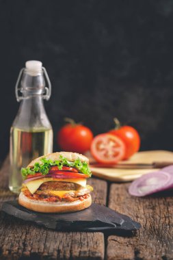 Marul, peynir, soğan ve domatesli lezzetli ev yapımı hamburgerler siyah taş ve ahşap arka planda.