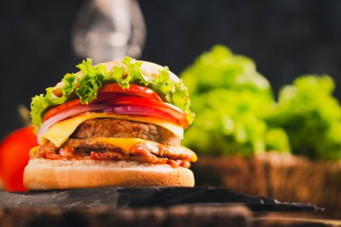 Siyah taş ve ahşap zemin üzerinde marul, peynir, soğan ve domatesli lezzetli ev yapımı hamburgerin yakın çekimi.