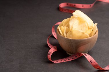 Ahşap bir kasede patates cipsi ve kahverengi arka planda kırmızı bant.