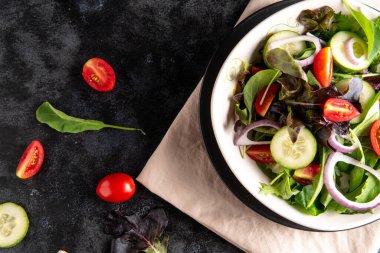 Taze marul, domates ve siyah arka planda beyaz tabakta salatalık ile sebze salatasını kapat.