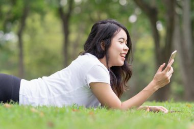 Genç kadın çimlerin üzerinde yatıyor ve akıllı telefondan arıyor..