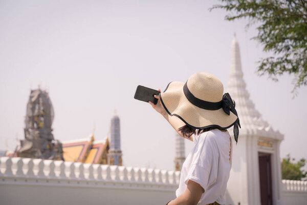 Portrait of Asian woman wearing a hat selfie with smartphone in Phra Kaew temple in Bangkok, Thailand.