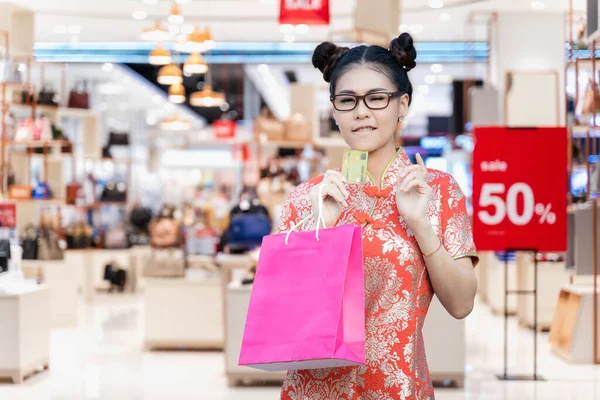 Portrait of beautiful Asian woman wearing red cheongsam and carrying shopping bag with credit card. Chinese New Year Festival which is a culture of Chinese nation and businese