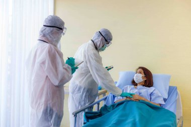 Koruyucu giysi ve maskeli erkek ve kadın doktorlar hastalık kontrol bölgesindeki kadın hastaların semptomlarını inceliyorlar. COVID 19 'u olan hastalara bakım ve tedavi kavramları.