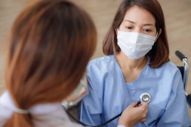 Asyalı kadın doktor, hastalık kontrol bölgesinde steteskop kullanan kadın bir hastanın semptomlarını kontrol ediyor. COVID 19 'u olan hastalara bakım ve tedavi kavramları.