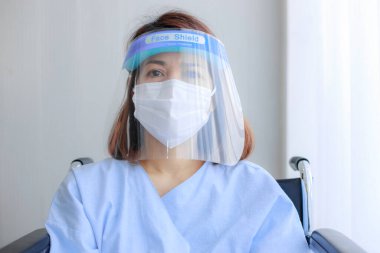 Hasta kıyafetleri giyip, maske takıp tekerlekli sandalyeye mahkum Asyalı kadın hastaları kapatın..