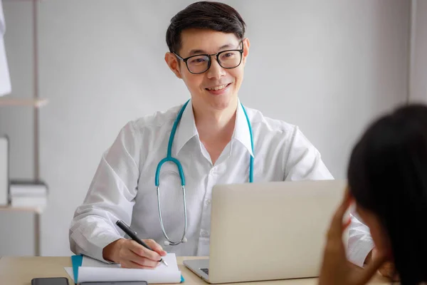 若いアジアの男性医師は クリップボードに医療史を記録し 女性患者に何かを説明しています ヘルスケアの概念 — ストック写真