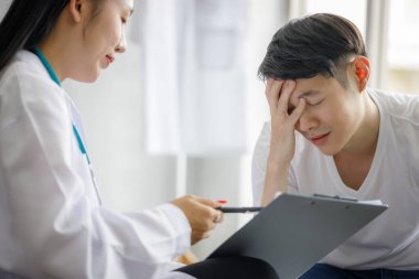 Güzel, genç, Asyalı bir bayan doktor panoya tıbbi bir geçmiş kaydediyor ve erkek hastaya bir şey anlatıyor. Tıbbi ve sağlık hizmetleri kavramları