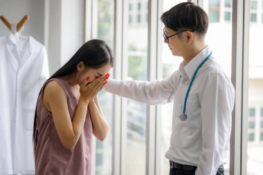 Asyalı erkek psikiyatrist, covid 19 'un yayılmasından endişe duyan genç bir kadını cesaretlendirmek için elini omzuna koyar. Hastalık belirtileri sağlık hizmetleri kavramını anlatıyor