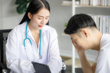 Güzel, genç, Asyalı bir bayan doktor panoya tıbbi bir geçmiş kaydediyor ve erkek hastaya bir şey anlatıyor. Tıbbi ve sağlık hizmetleri kavramları