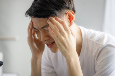 Genç Asyalı adam COVID 19 virüsü salgını sırasında karantinaya alındığı için endişeli ve baş ağrısı çekiyor. Evde kal. Ruh sağlığı sorunları.