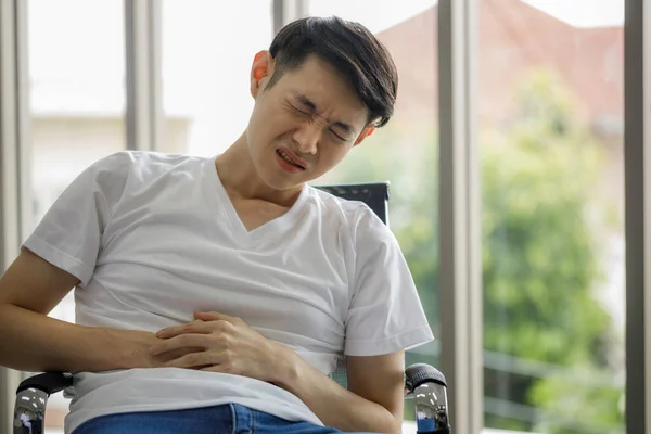 Ung Asiatisk Man Sitter Magen Med Handen Stol Hemmet Grund — Stockfoto
