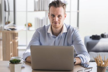 Ev ofisinden sabah güneşiyle çalışan genç bir adamın portresi. Sosyal ağda iletişim kuran ve çevrimiçi bilgi arayan mutlu adam.