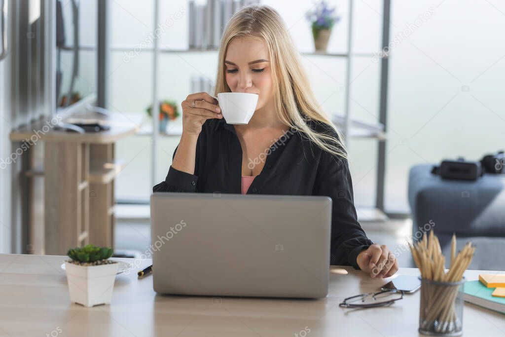 Young business woman working from home-office with morning sunshine. woman drinking coffee and using laptop for communicating in social network and searching information online.